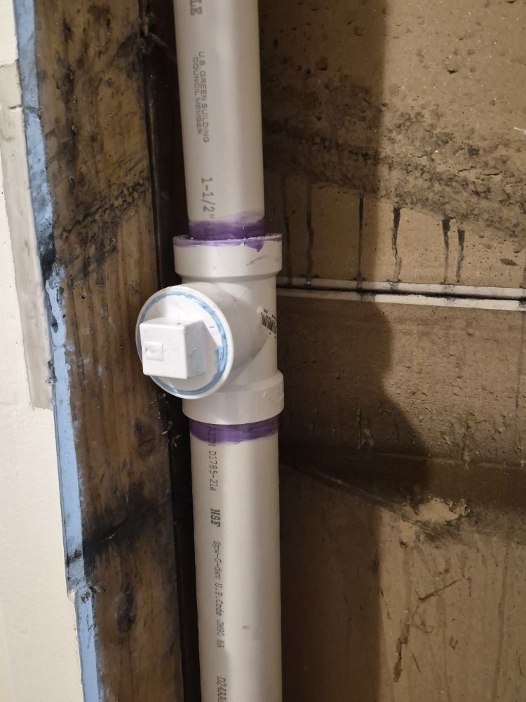 White PVC pipe with a sensor fitting mounted against a stained wall indoors