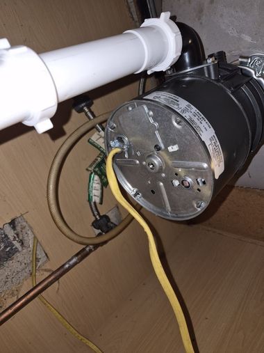 Black motor attached to white pipe inside a cardboard cabinet, with yellow and green wires visible.