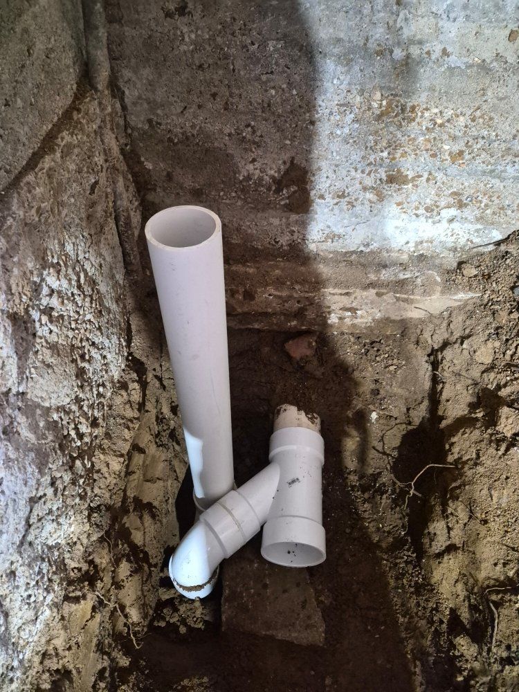 White PVC pipes in a rough concrete pit, with one vertical pipe and a connected elbow joint.