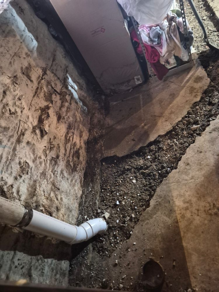 Narrow alley with cracked walls, exposed white pipe, and a muddy drainage trench running along the ground.