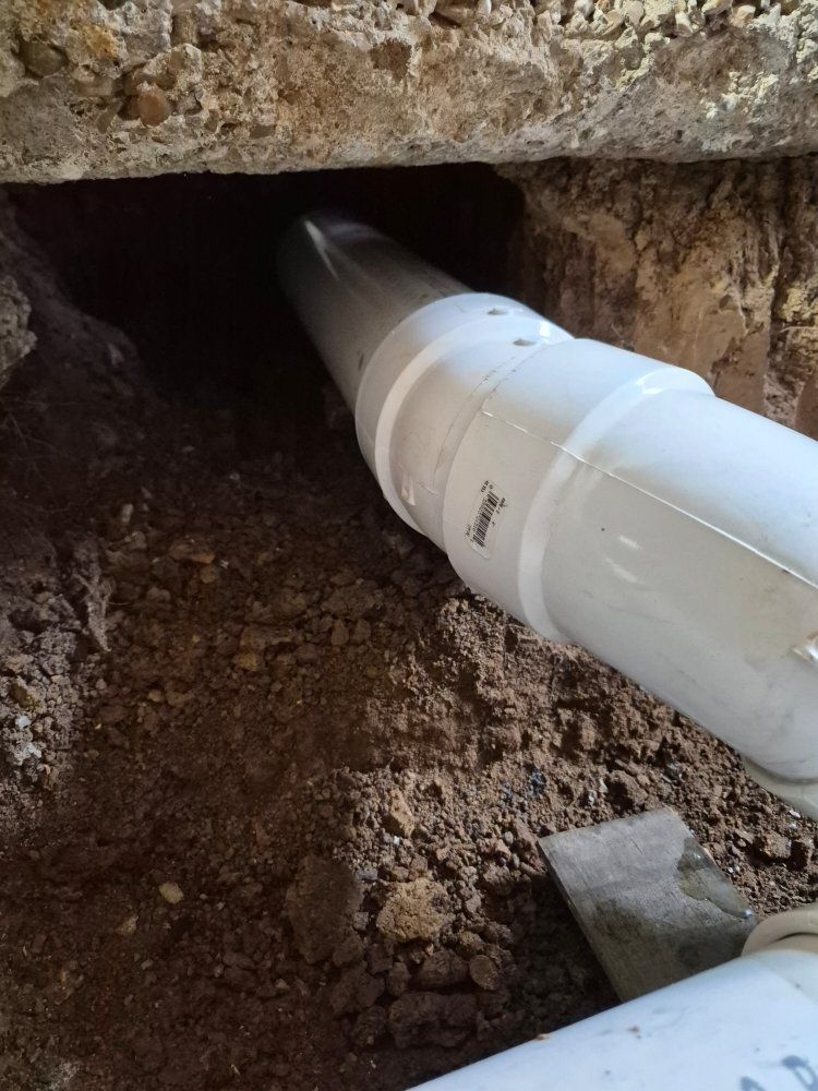 White PVC pipe inserted into a dirt hole beneath a concrete slab during repair work