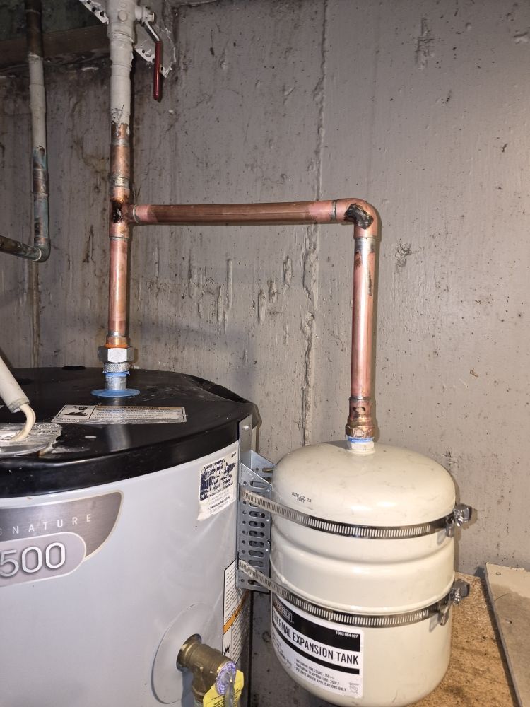 Copper pipes connected to two water heater tanks in a concrete utility room