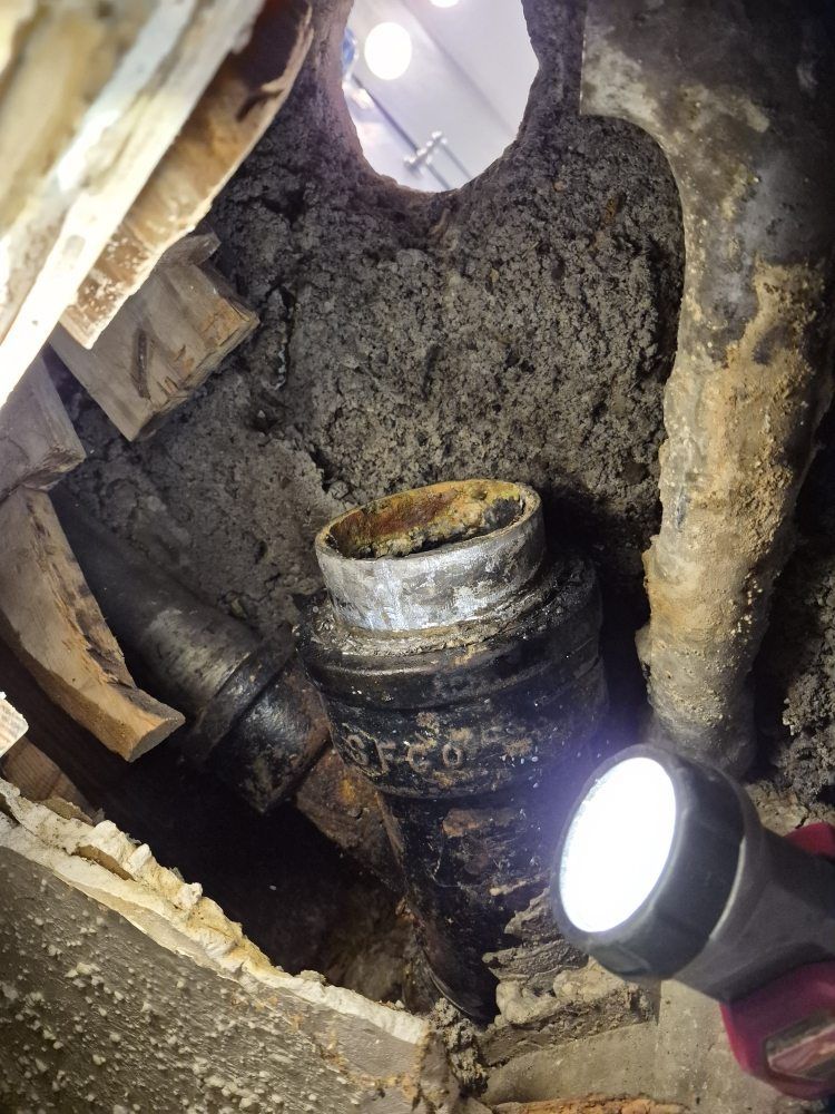 Broken underground pipe in a dirt-filled cavity, illuminated by two flashlights.