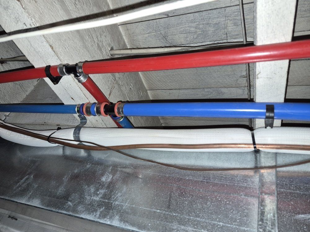 Red and blue pipes running along a ceiling with gray insulation and metal supports