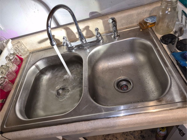Kitchen sink with two basins, running faucet, and a dish brush on the right.