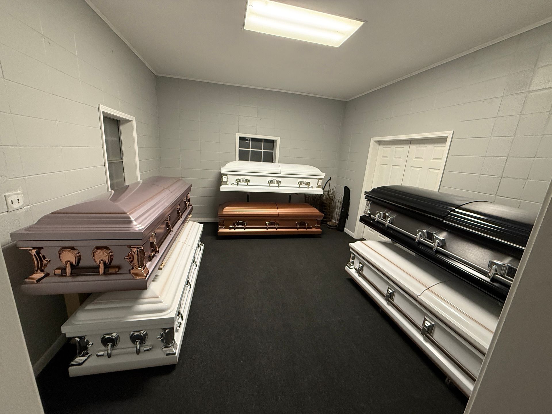 Coffins stored in a gray room on racks along the walls, with white and black caskets visible.