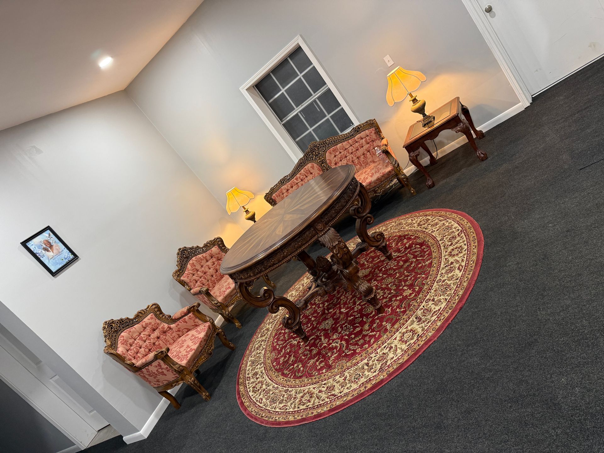 Elegant room with a round table, floral chairs, lamps, and a patterned rug on a gray carpet.
