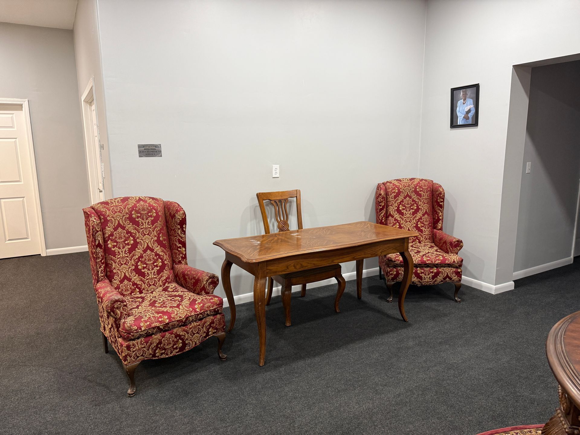 Small seating area with two red armchairs, a wooden table, and a wall-mounted TV in a plain room