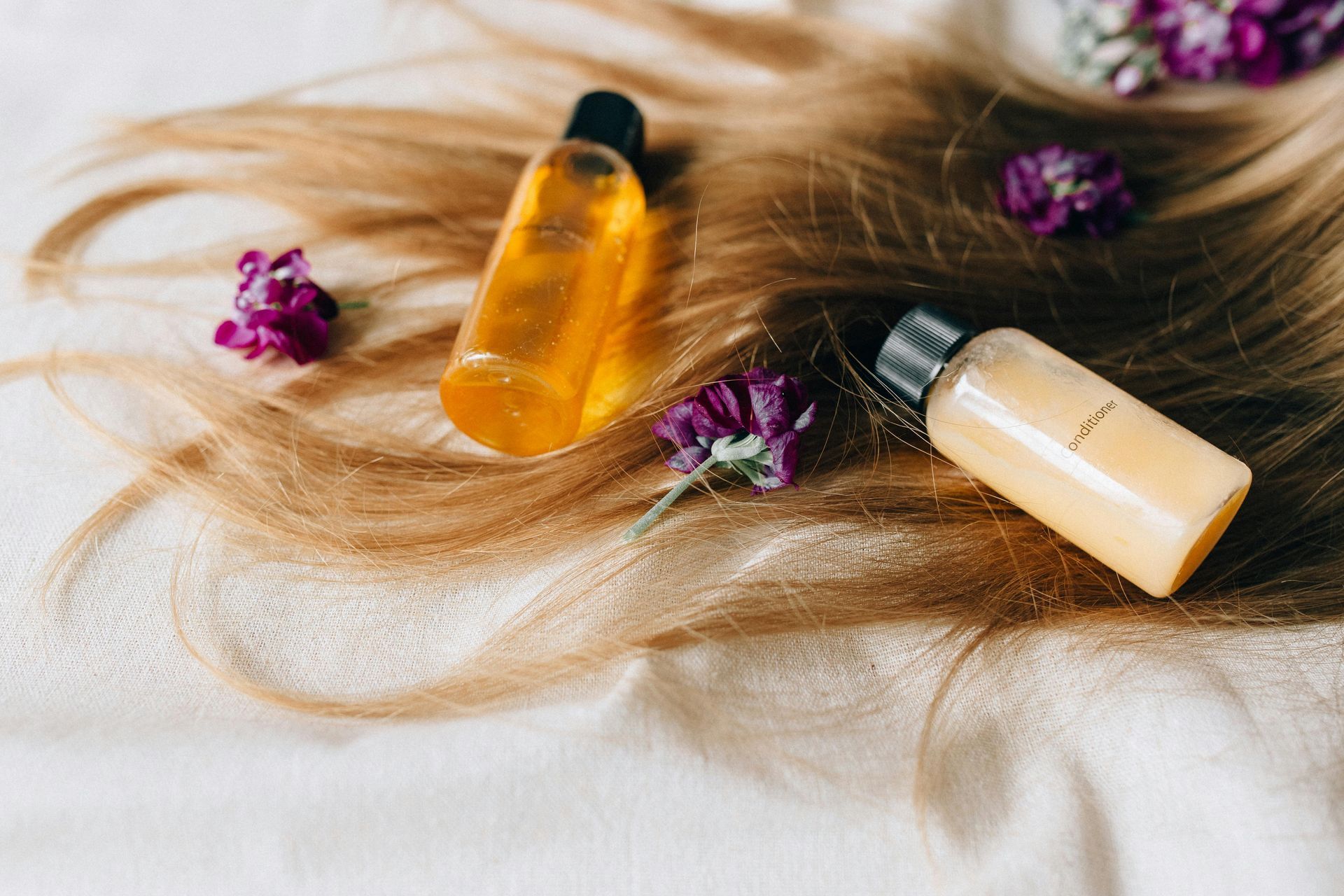 A close up of a woman 's hair with two bottles of shampoo and flowers.
