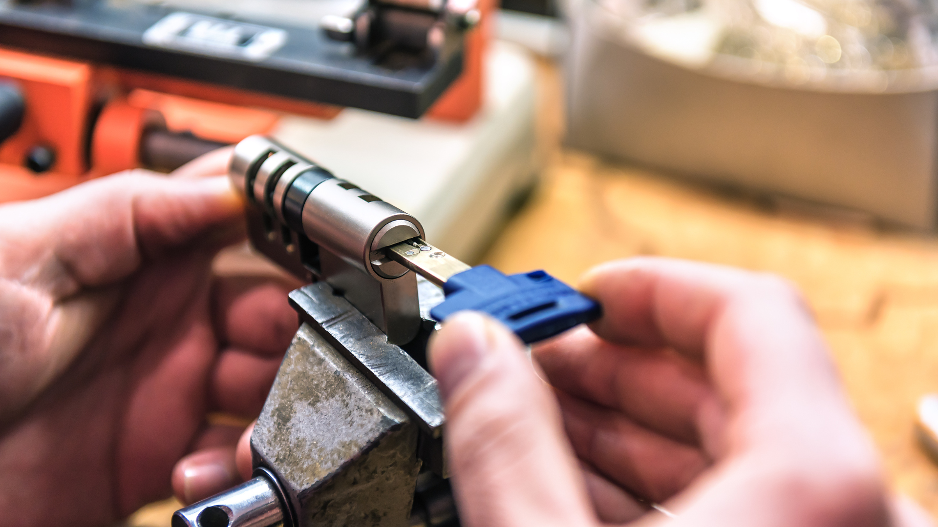Hands using a clamp to hold a metal cylinder while adjusting a blue connector on a workbench