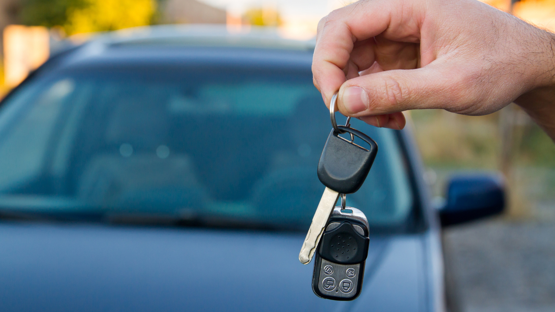 Hand holding car keys in front of a parked car, ready to drive