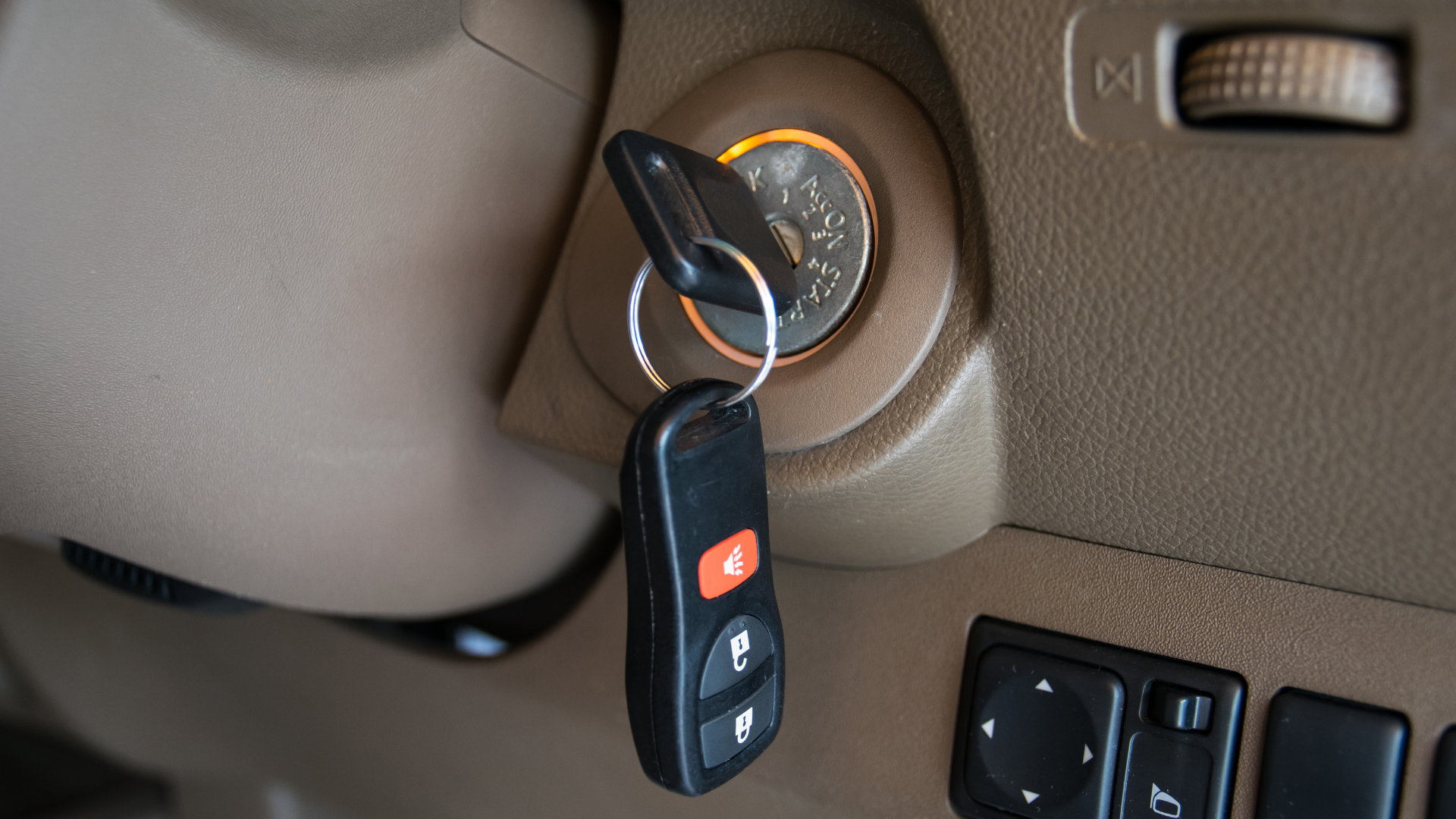 Car key in ignition of a car dashboard, with a black key fob hanging below.