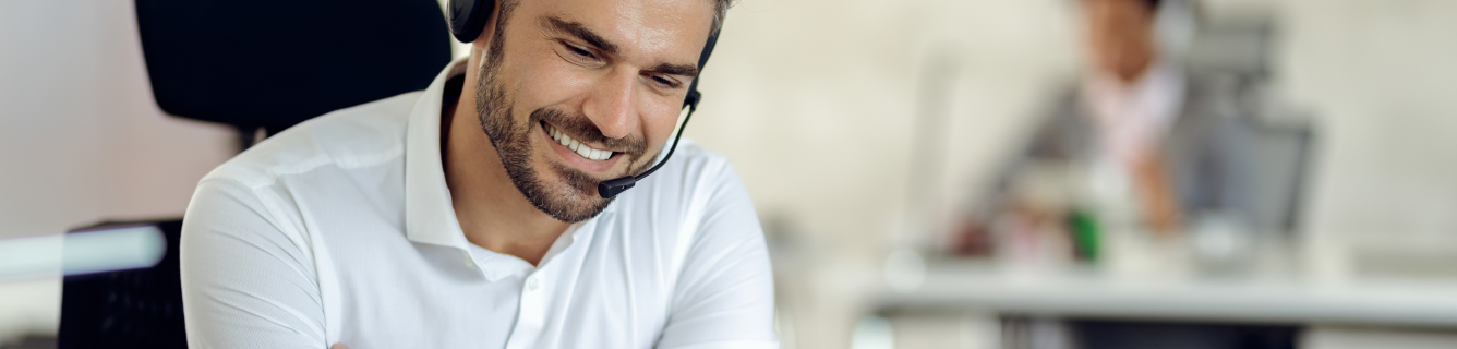 Um homem está usando um fone de ouvido e sorrindo enquanto fala ao telefone.