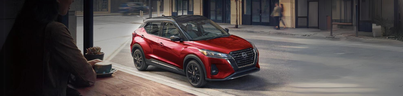 Um Nissan Kicks vermelho está estacionado na beira de uma rua da cidade.