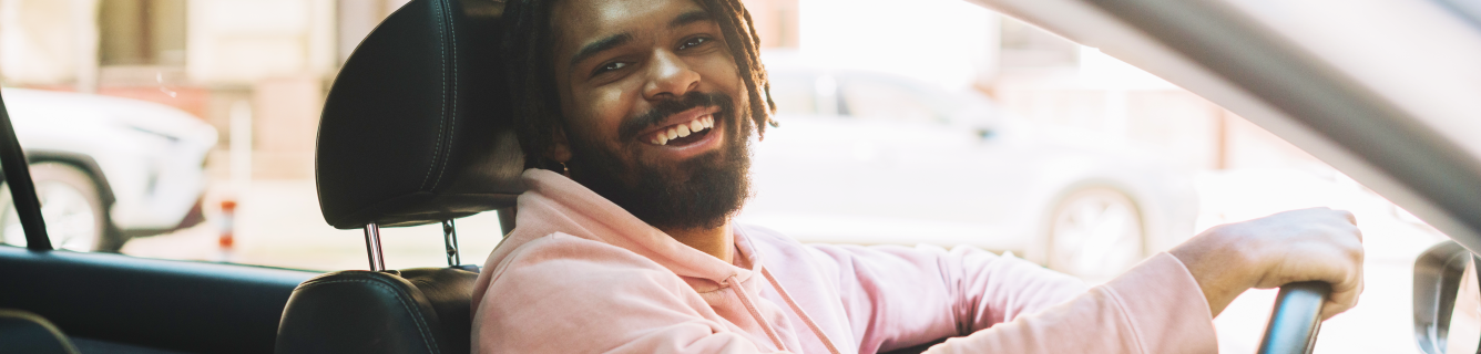 Um homem com dreadlocks está dirigindo um carro e sorrindo.