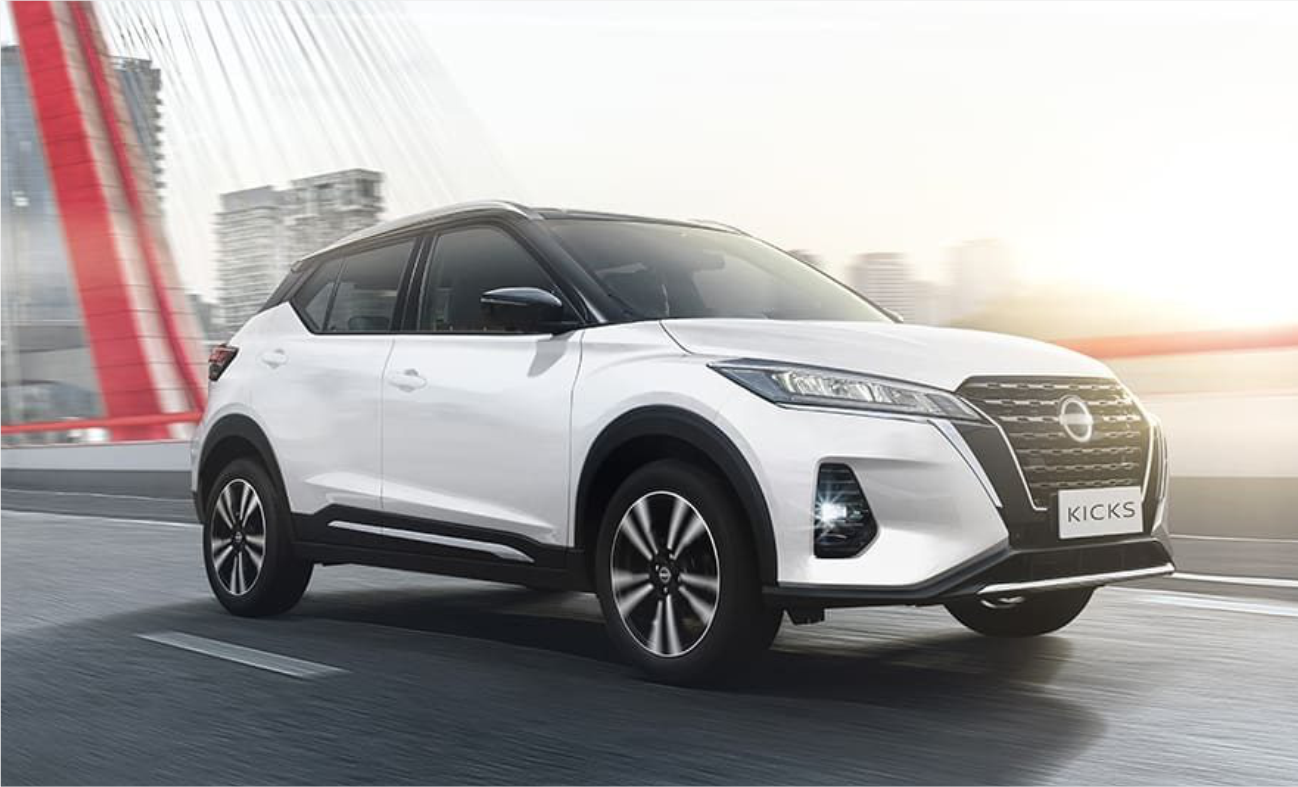 Um Nissan Kicks branco está estacionado na beira da estrada, em frente a uma ponte.
