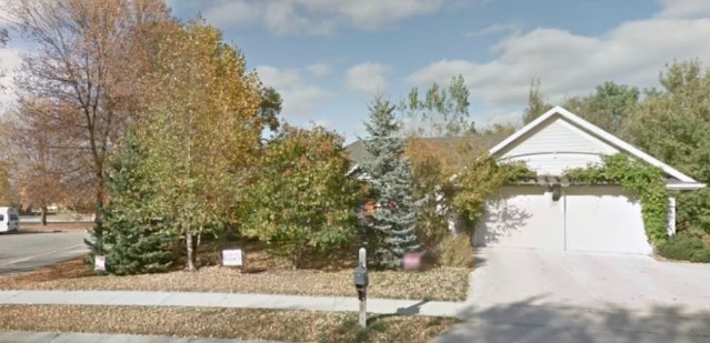 A white house with a garage is surrounded by trees on a sunny day.