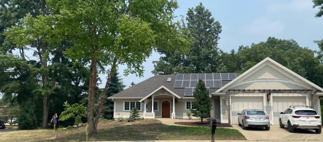 A house with two cars parked in front of it and solar panels on the roof.