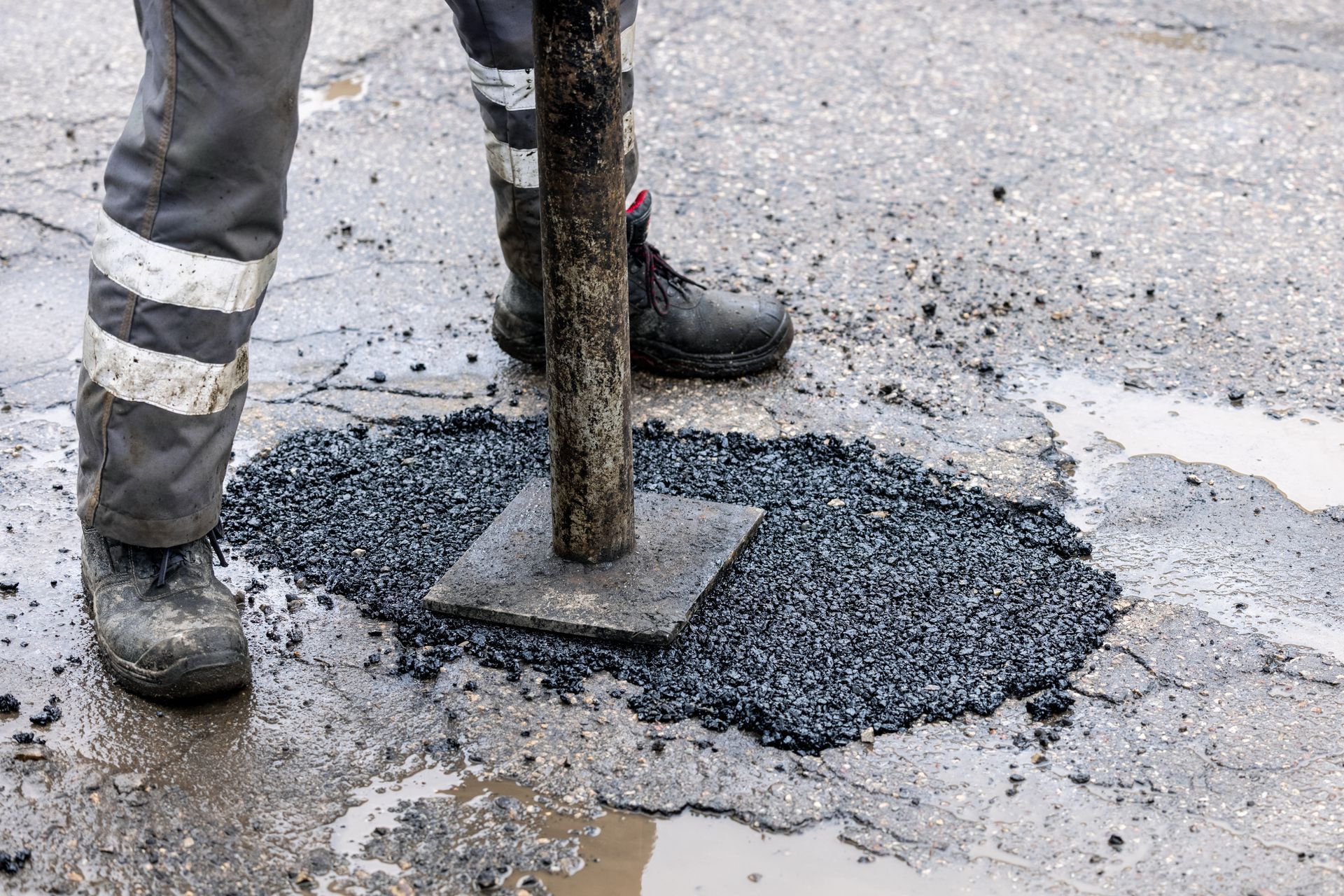 Worker repairs a pothole by spreading bitumen into a damaged section of road.