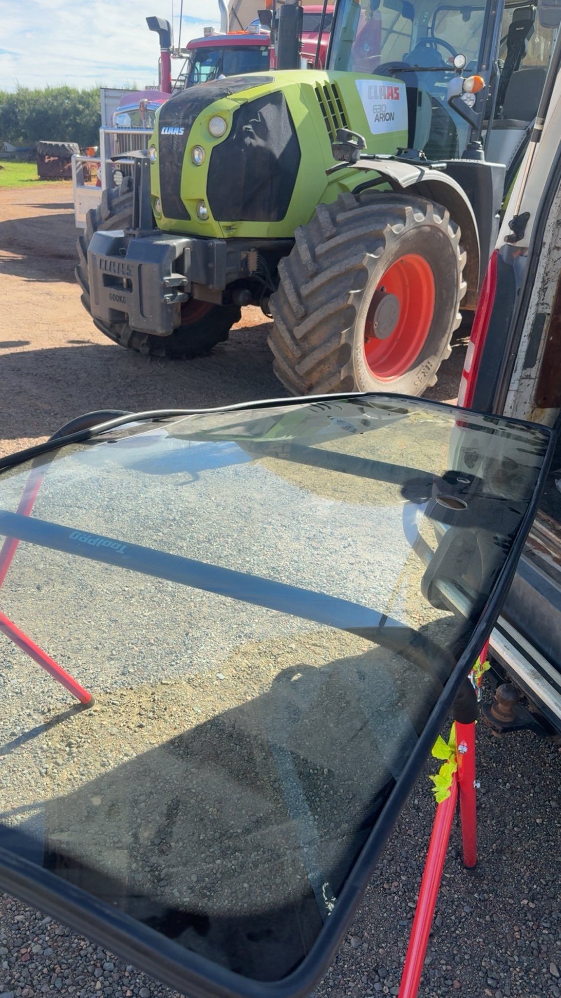 A Large, Curved Glass Tractor Windshield Rests on a Stand Outdoors — Far North Windscreens in Mareeba, QLD