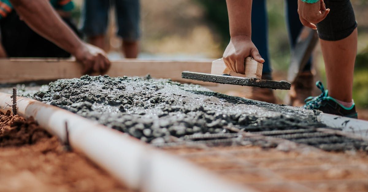 Workers leveling wet concrete in a wooden form during construction.