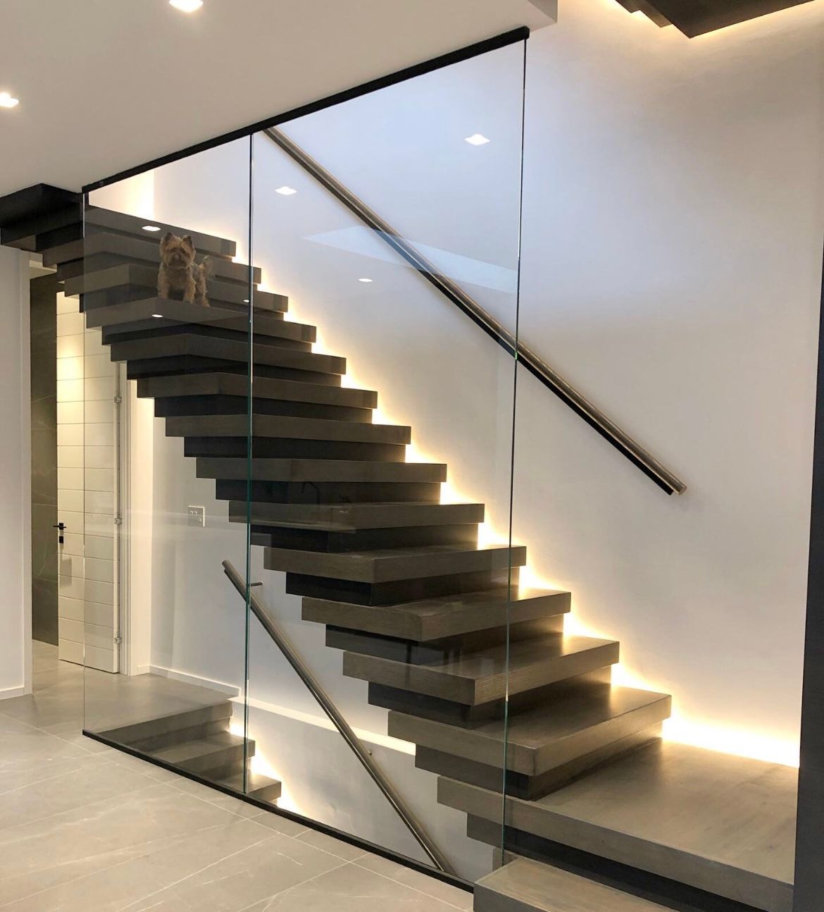 Escalier flottant avec garde-corps en verre et éclairage intégré dans une maison moderne.