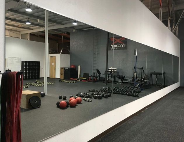 Grand espace de gym avec mur miroir, poids et équipement d'exercice.
