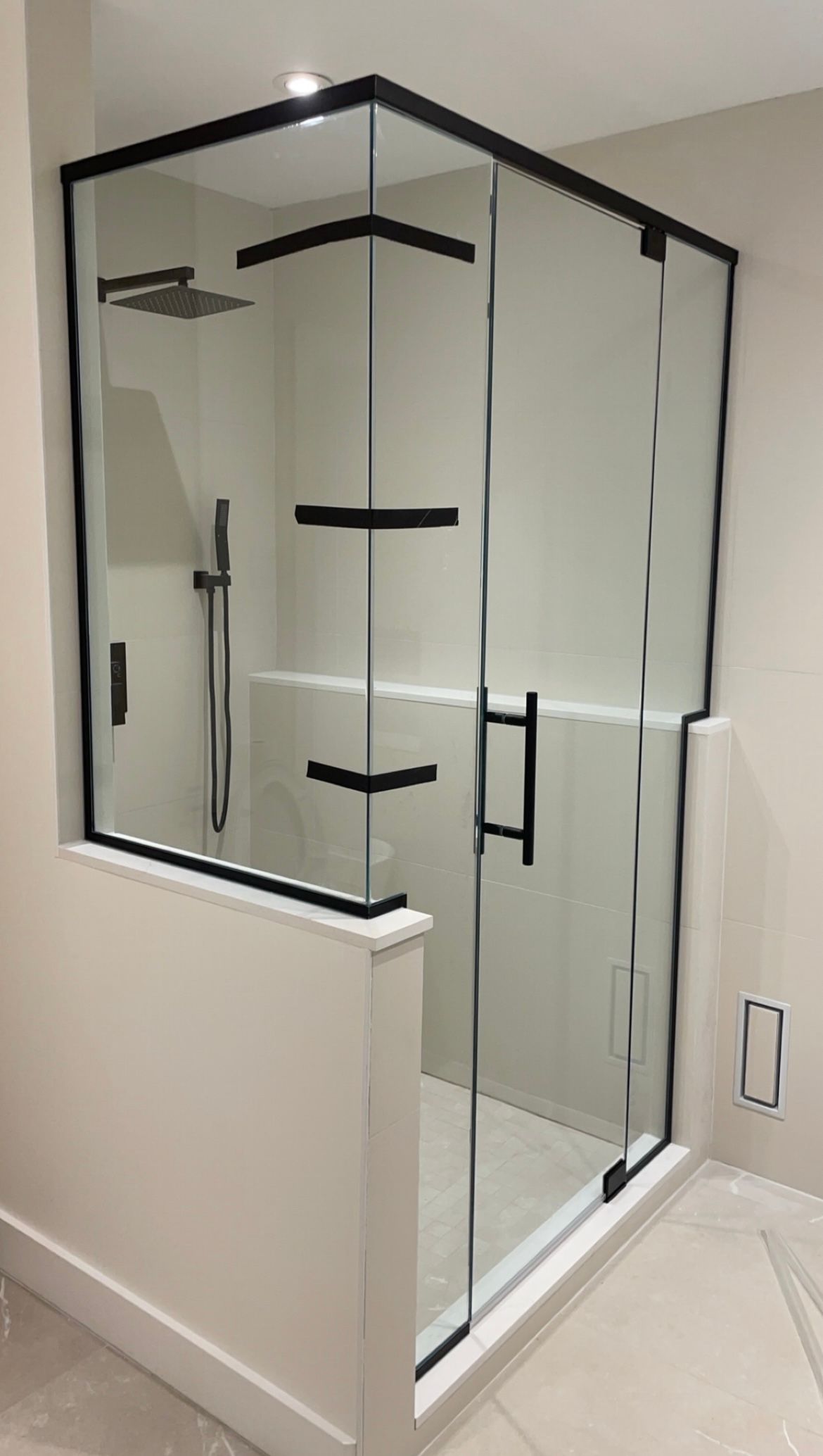 Douche en verre moderne avec garniture et quincaillerie noires, à côté d'un mur blanc.