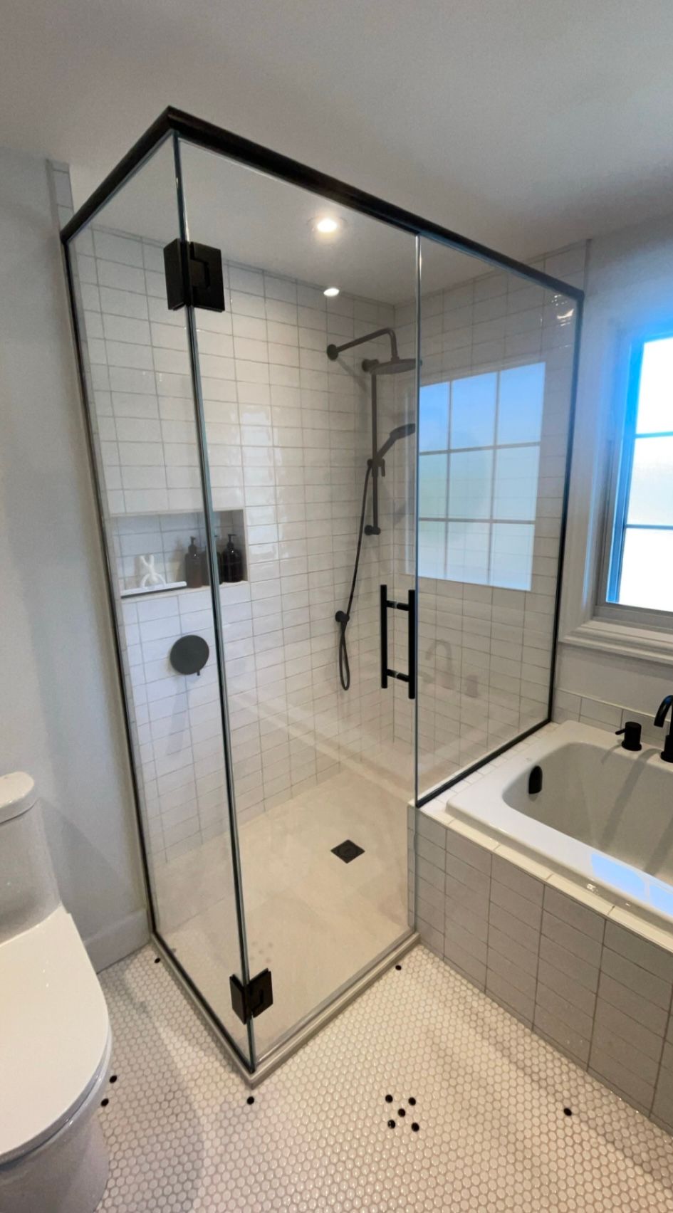 Salle de bain moderne avec douche en verre à cadre noir, murs en carrelage métro blanc et baignoire.