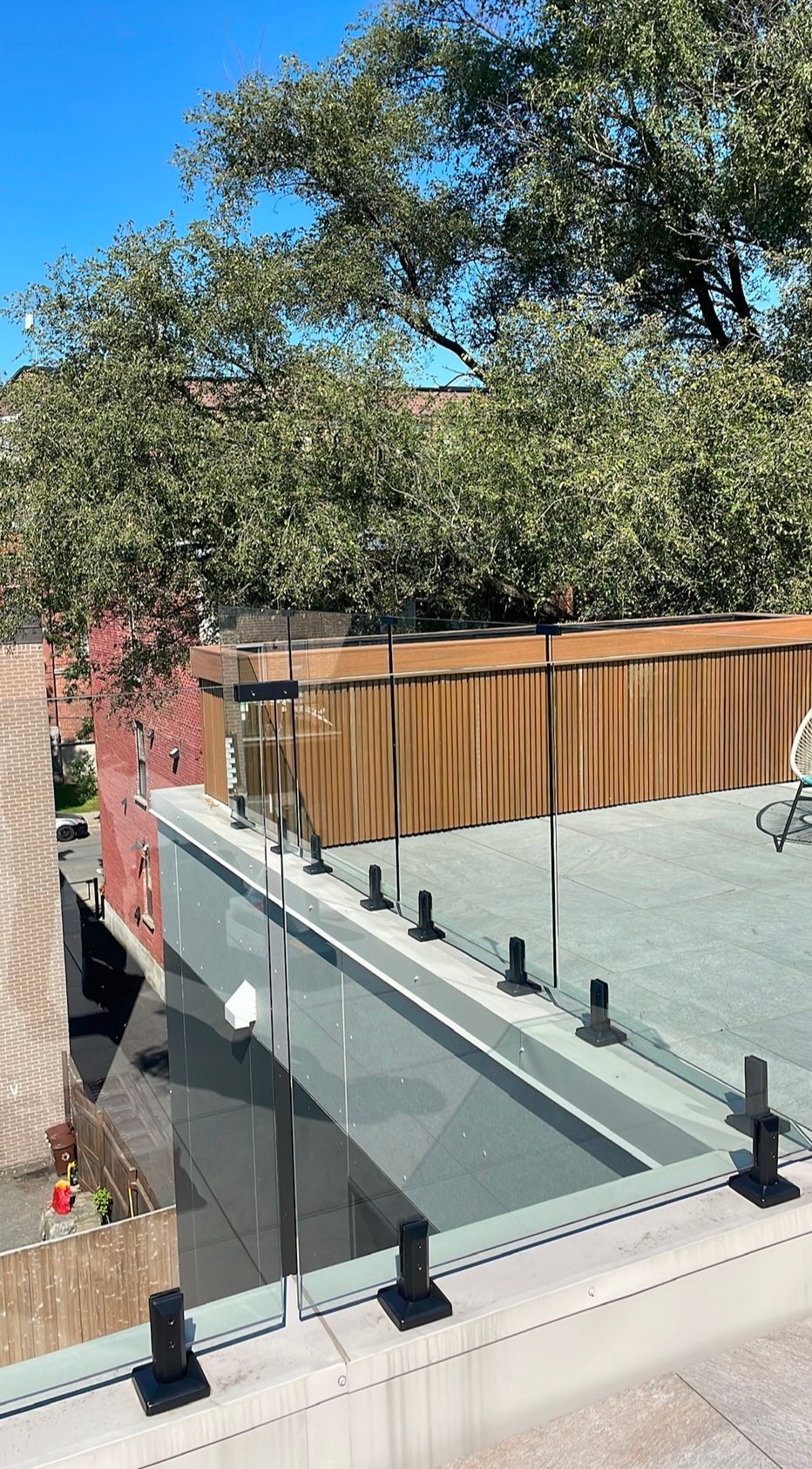 Toit moderne avec balustrade en verre, boiseries et arrière-plan d'arbres luxuriants contre un ciel bleu.