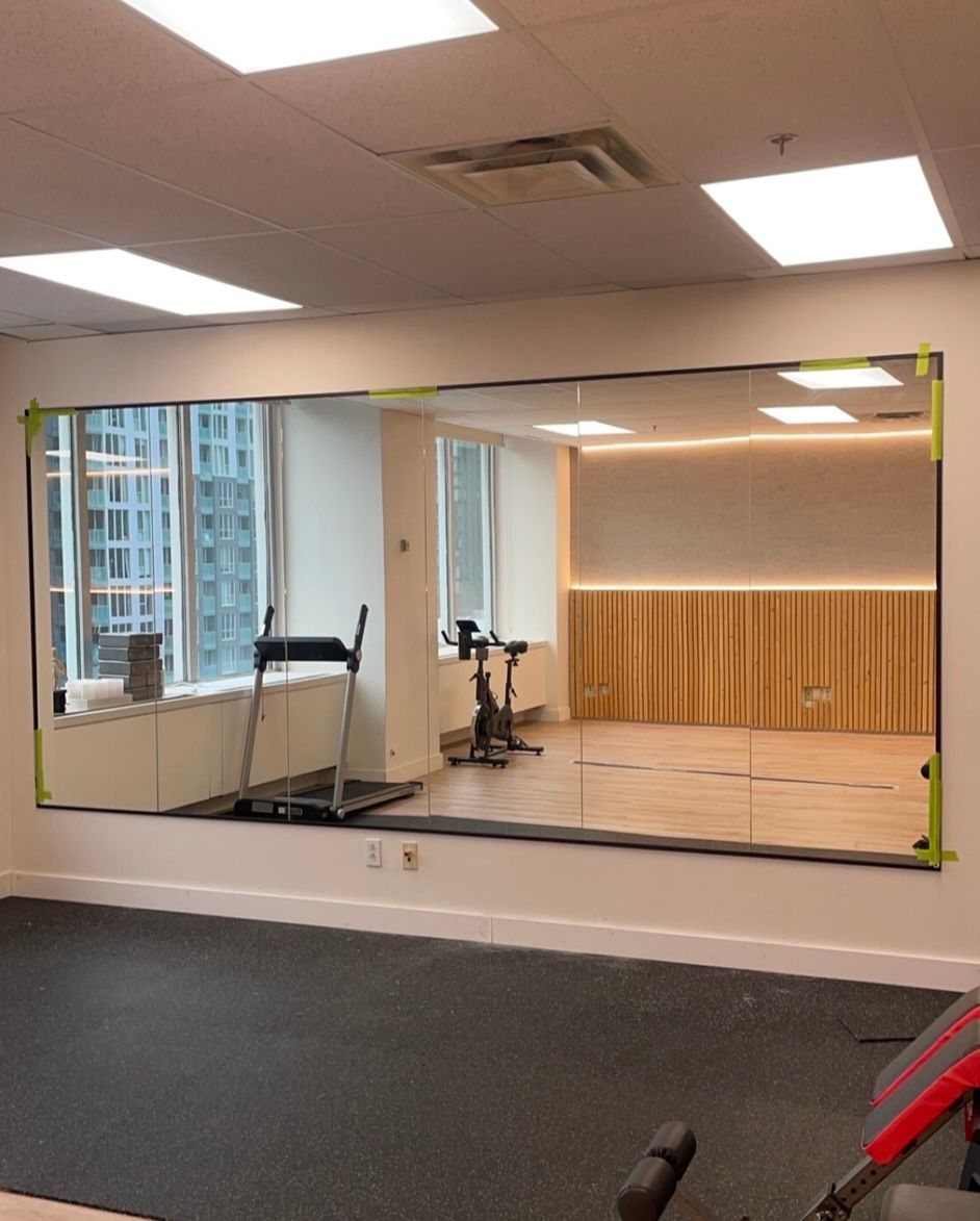 Grand miroir sur le mur d'une salle de sport, reflétant l'équipement d'exercice et une vue d'une ville à travers les fenêtres.
