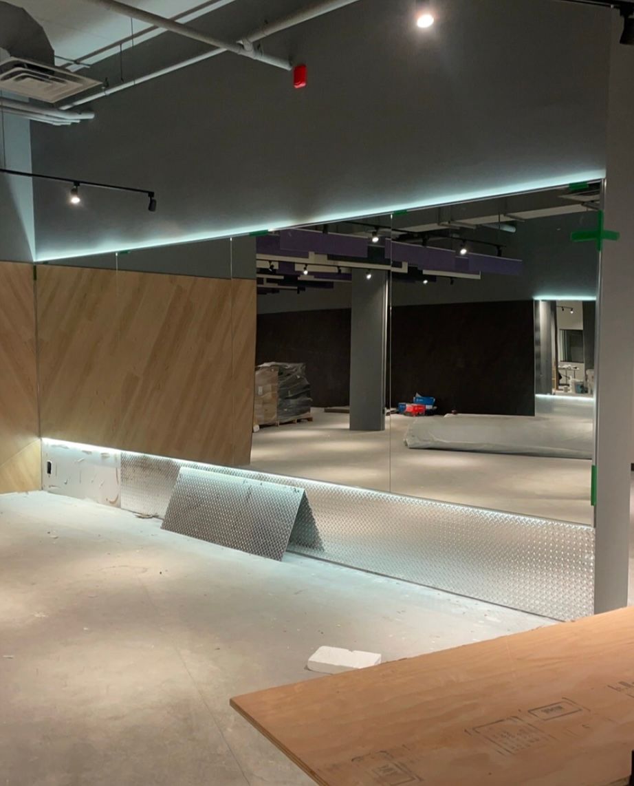 Vue intérieure d'un espace commercial vide en construction. Grand miroir, boiseries, plafond gris et carrelage blanc.