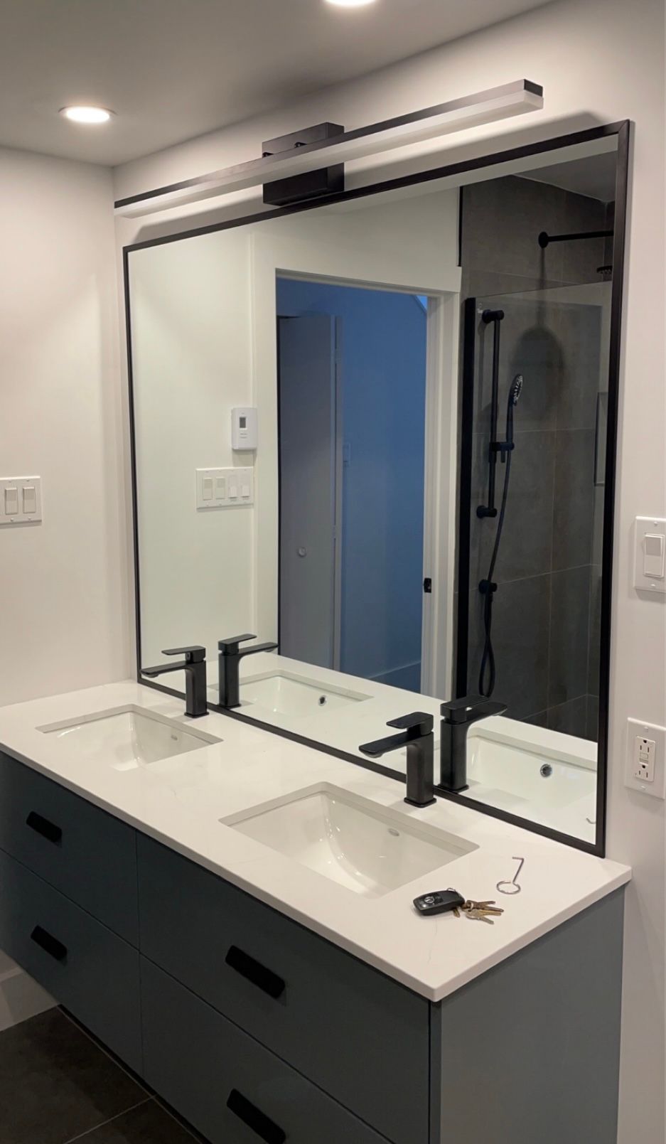 Meuble-lavabo de salle de bain avec un grand miroir, des luminaires noirs et des armoires bleues.