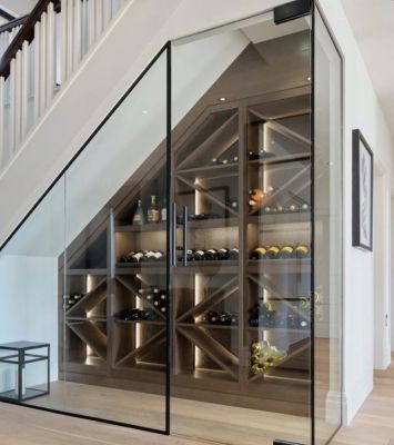 Cave à vin sous escalier avec porte vitrée, étagères en bois et éclairage intégré.