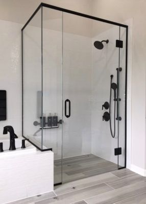 Douche en verre à cadre noir avec accessoires noirs; sol en carrelage gris, murs blancs.