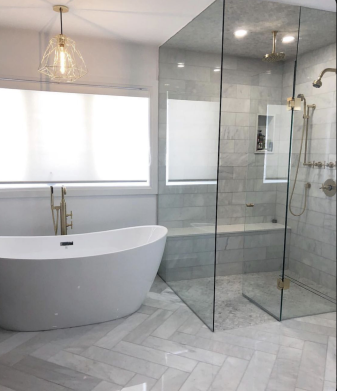 Salle de bain moderne avec baignoire blanche, douche en verre, carrelage en marbre et luminaires dorés.