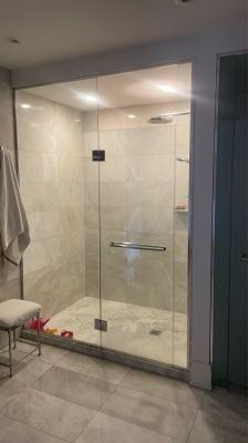 Cabine de douche en verre avec murs carrelés, porte-serviettes sur un support et tabouret.
