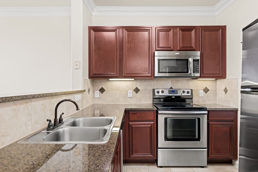 Apartment kitchen with double sink, stainless steel appliances and wooden cabinets at Marquis Rockwall in Rockwall, TX.