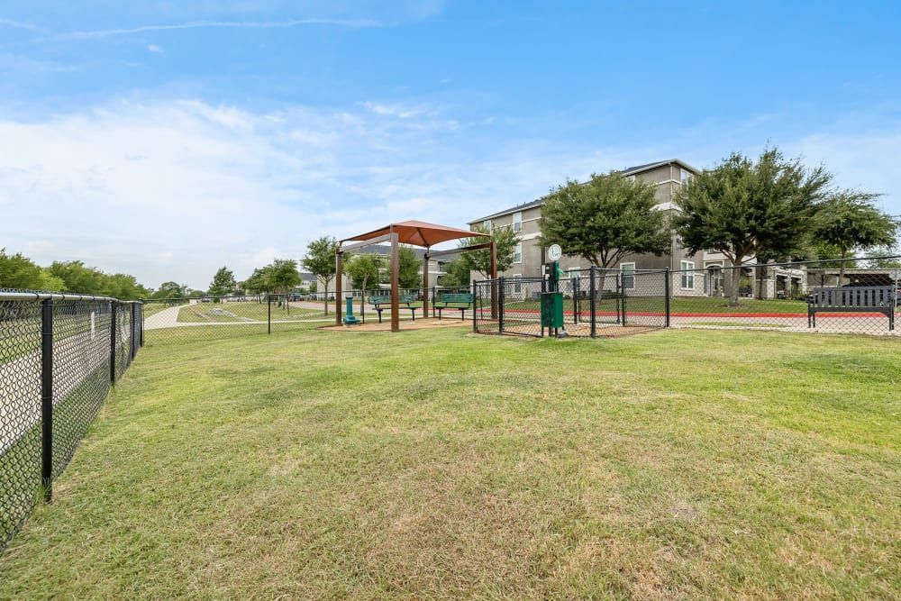 A large grassy field with a fence and a playground at Marquis Rockwall in Rockwall, TX.