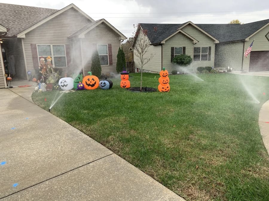 Halloween lawn decorations on a suburban front yard, with pumpkins, ghosts, and a skeleton by the house.