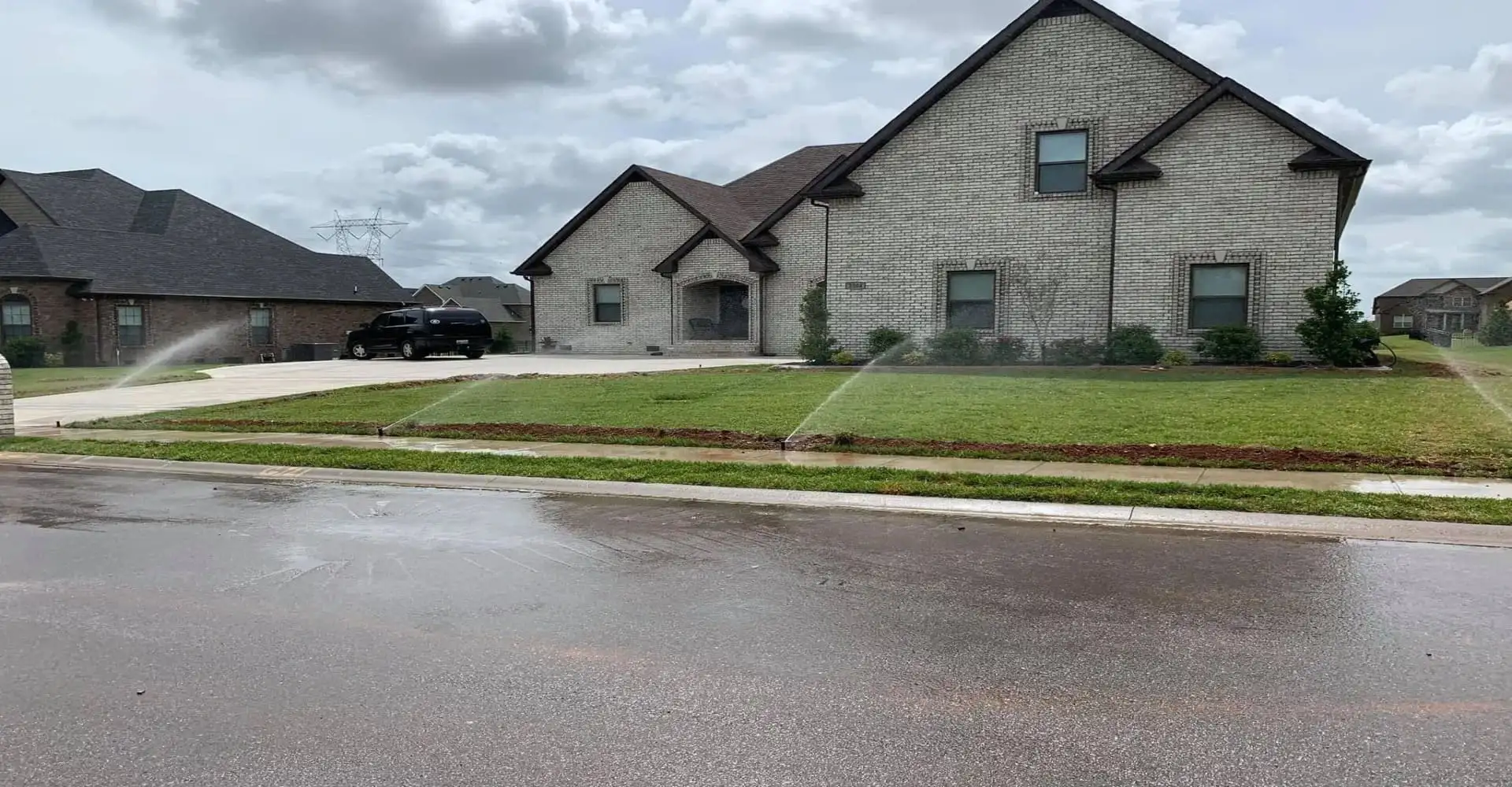 Suburban houses along a wet street with green lawns under an overcast sky