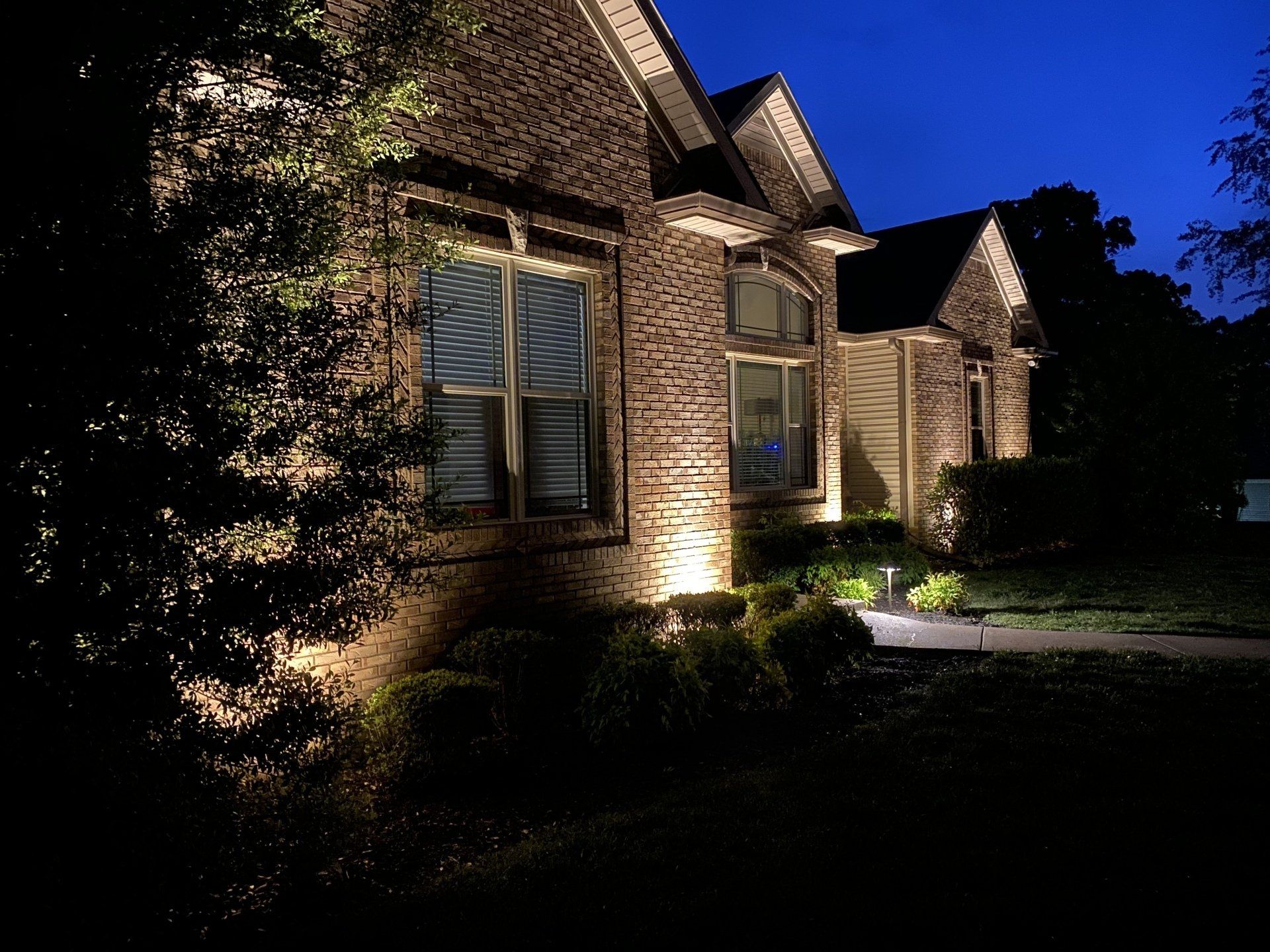 Brick house at night with warm exterior lighting and a lit walkway in front