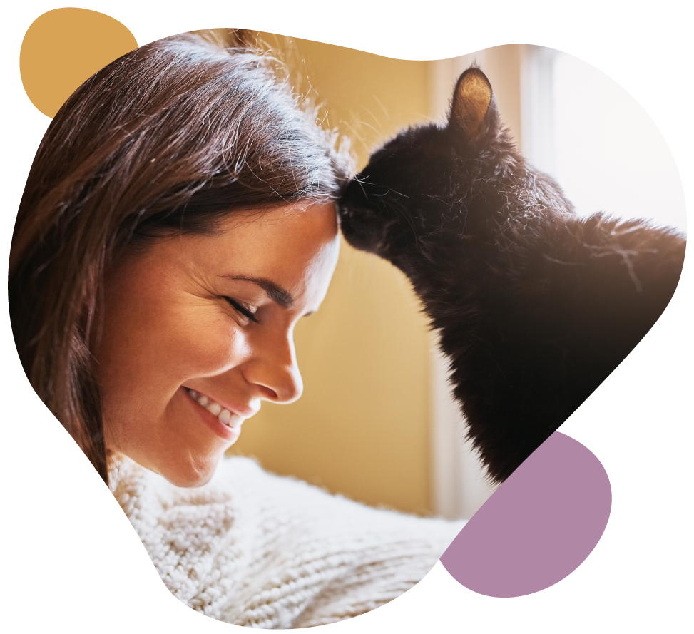 Woman smiling nose-to-nose with a black cat, framed by a heart-shaped cutout on a soft background