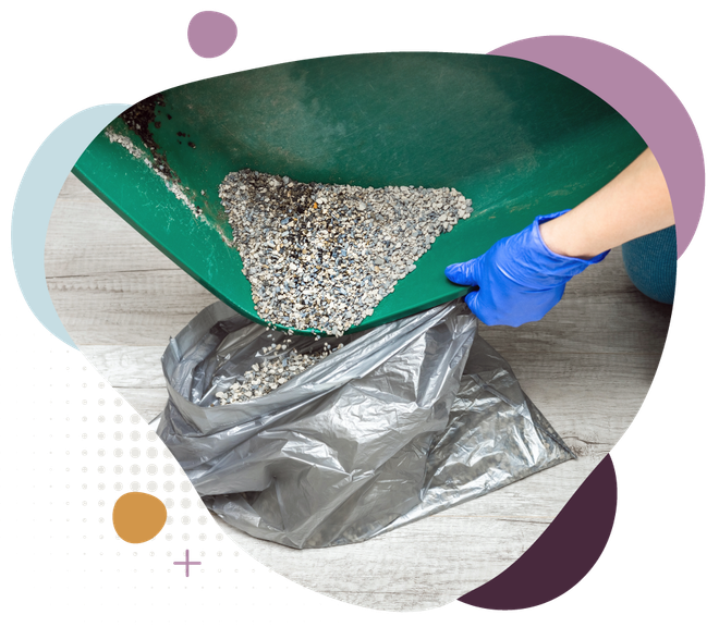 Blue-gloved hand empties gravel from a green wheelbarrow into a gray trash bag