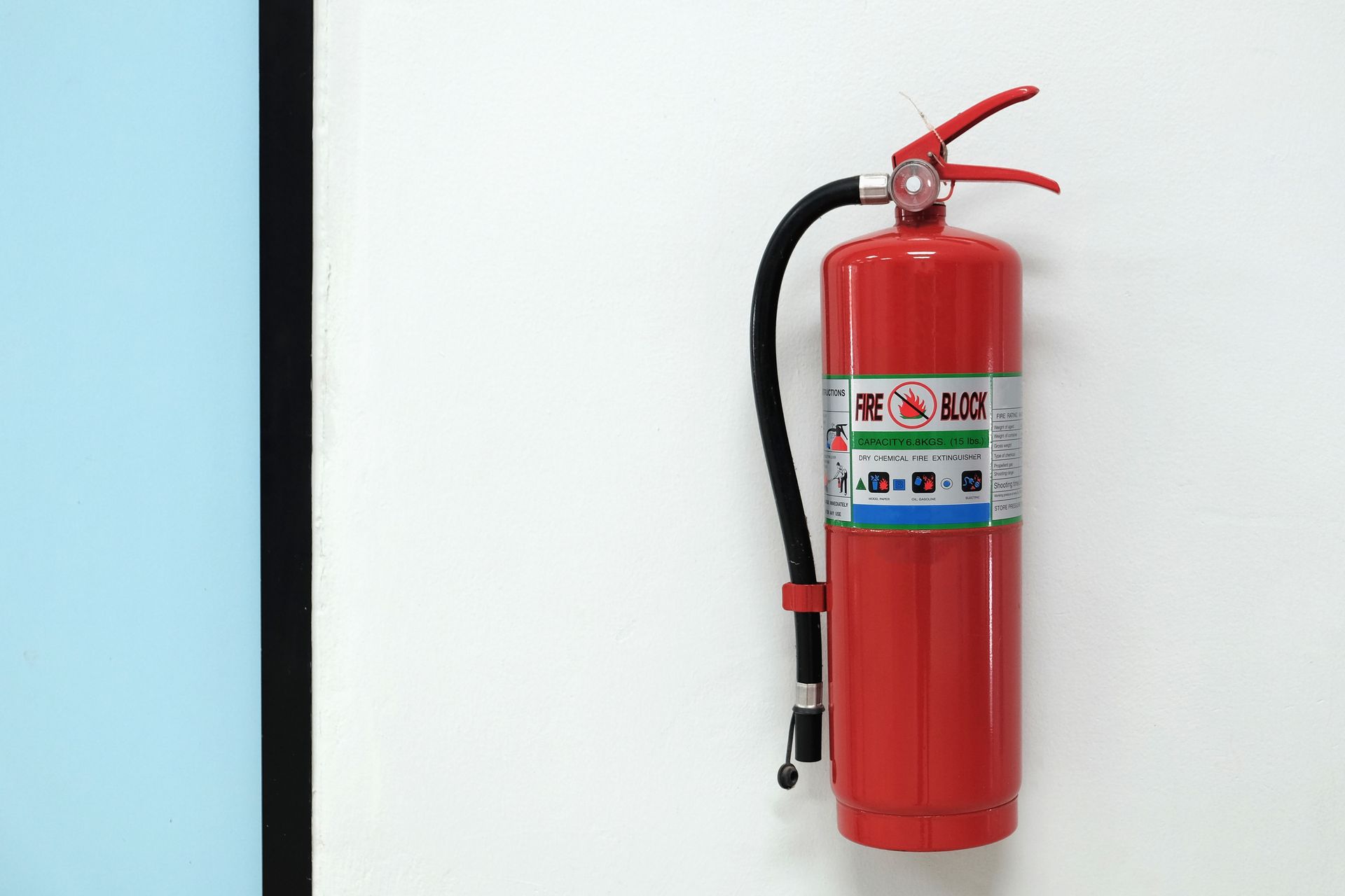 Red dry chemical fire extinguishers mounted on a white wall with hose, pull pin and service label.