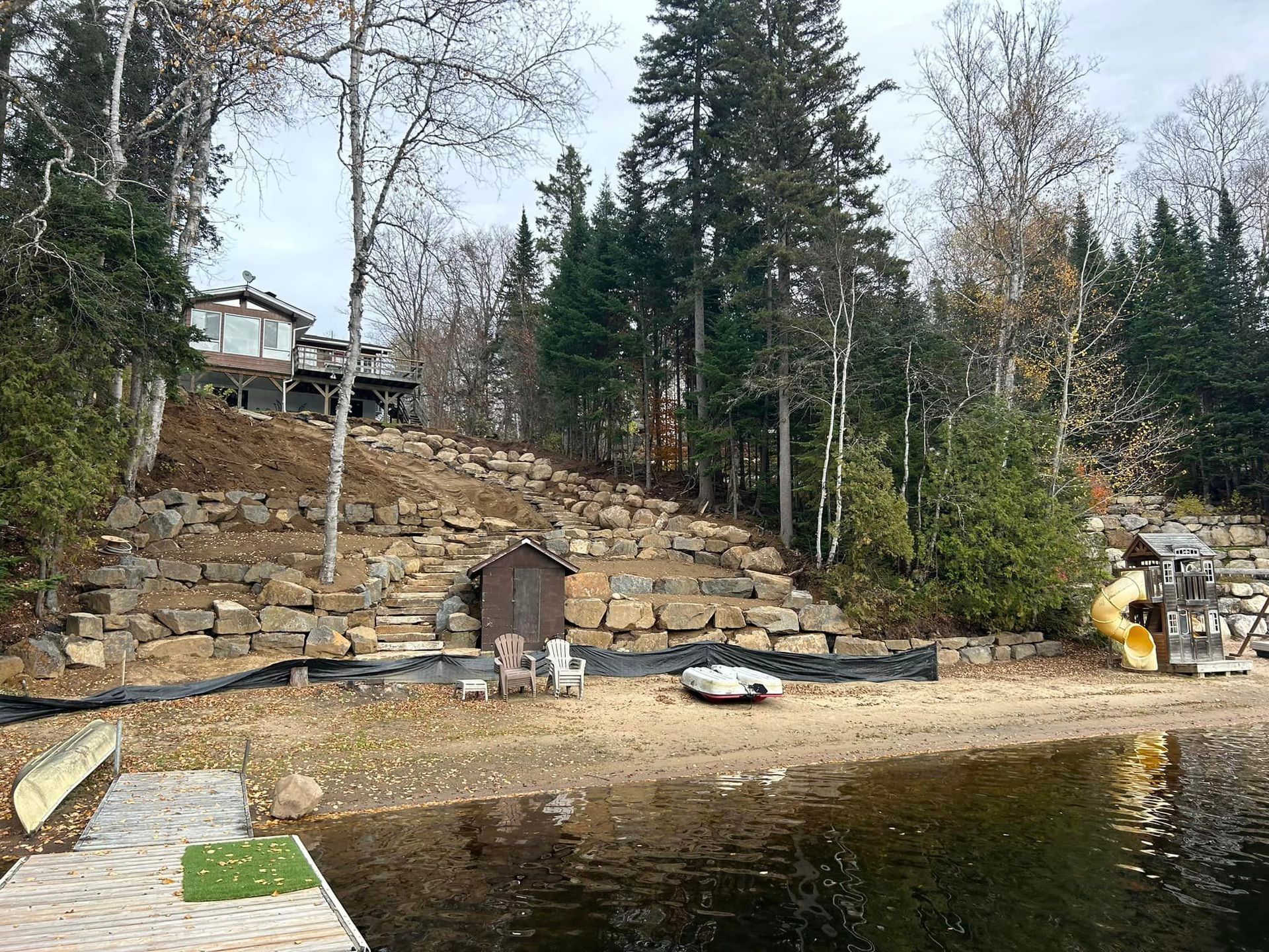 Une maison est assise au sommet d'une colline à côté d'un lac entouré d'arbres.