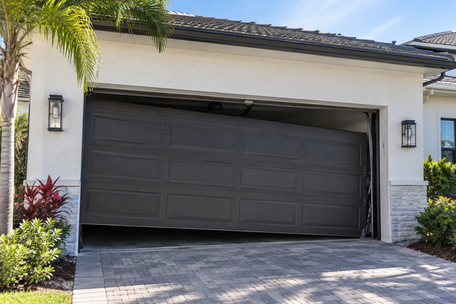 Partially open dark gray garage door on a white stucco house with a tiled roof and landscaped entry