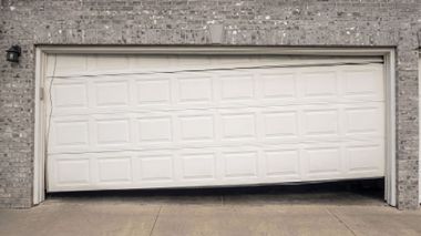 White garage door under leafy vines and a tiled roof, with shadows cast across it.