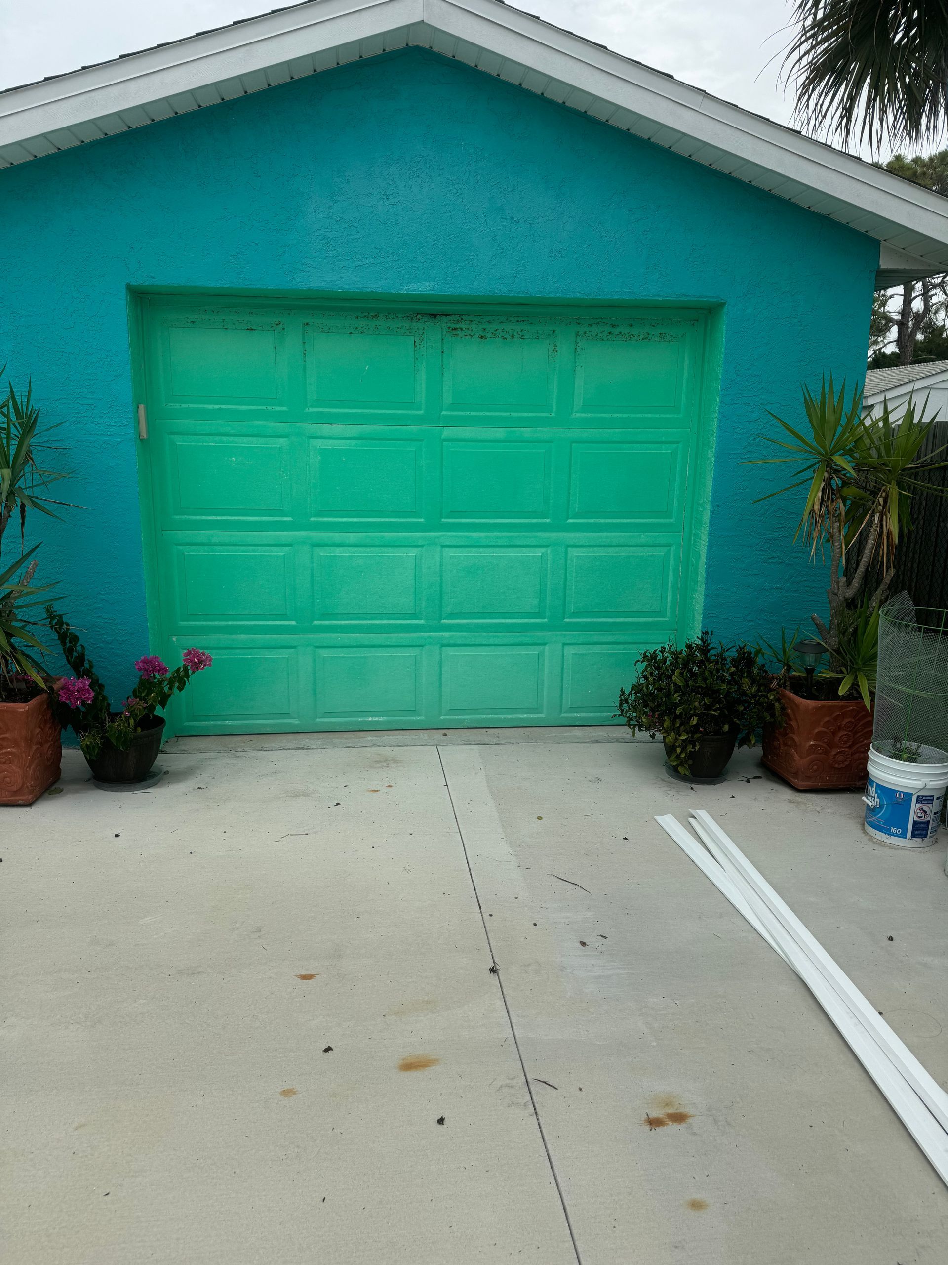 Turquoise garage with matching door, concrete driveway, and potted plants on either side