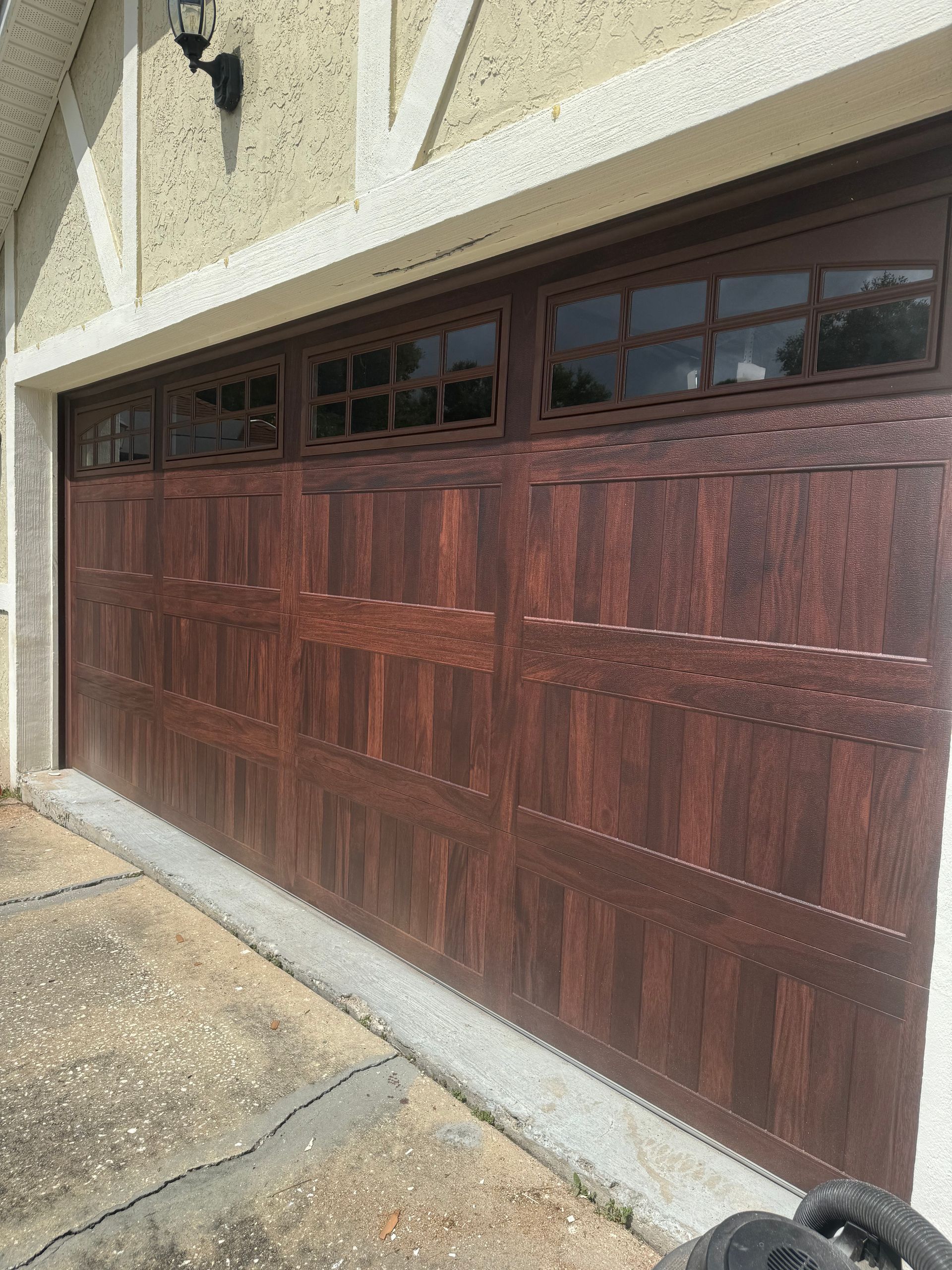 Wood-paneled garage door with small windows beneath a stucco exterior wall